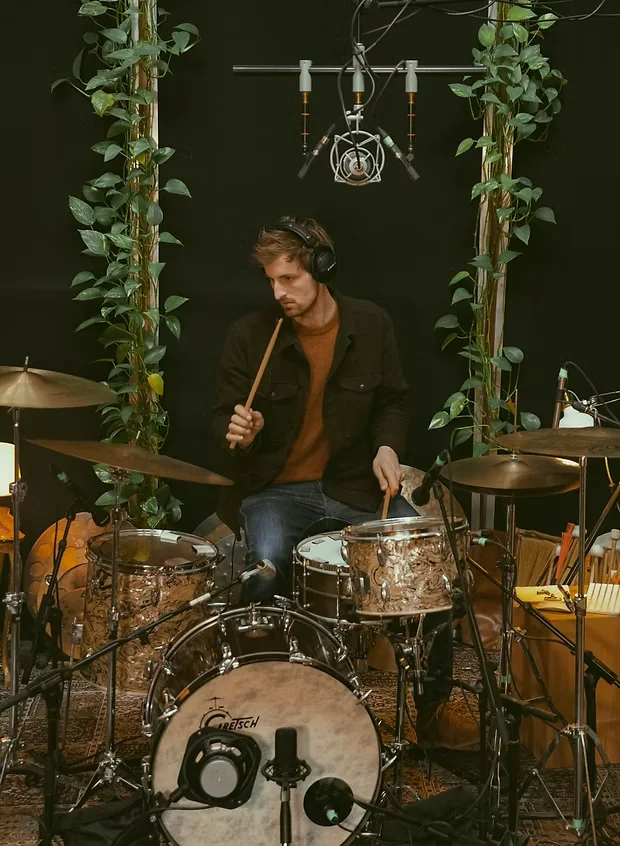 Alex Höffken behind his drum kit, headphones on, sticks in hand, overhead microphones above him